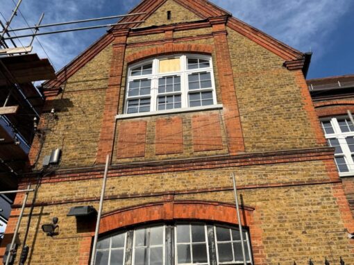 Gable end, scaffolding up, boarded panel in upper window, grimy dark frames