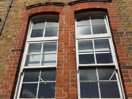 Two tall arched windows, flaking paint, decayed timber sills